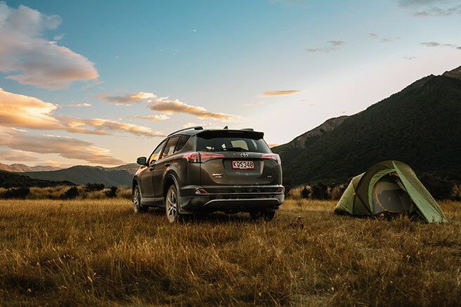 A GO Rentals Toyota RAV4 parked beside a tent at dusk in New Zealand